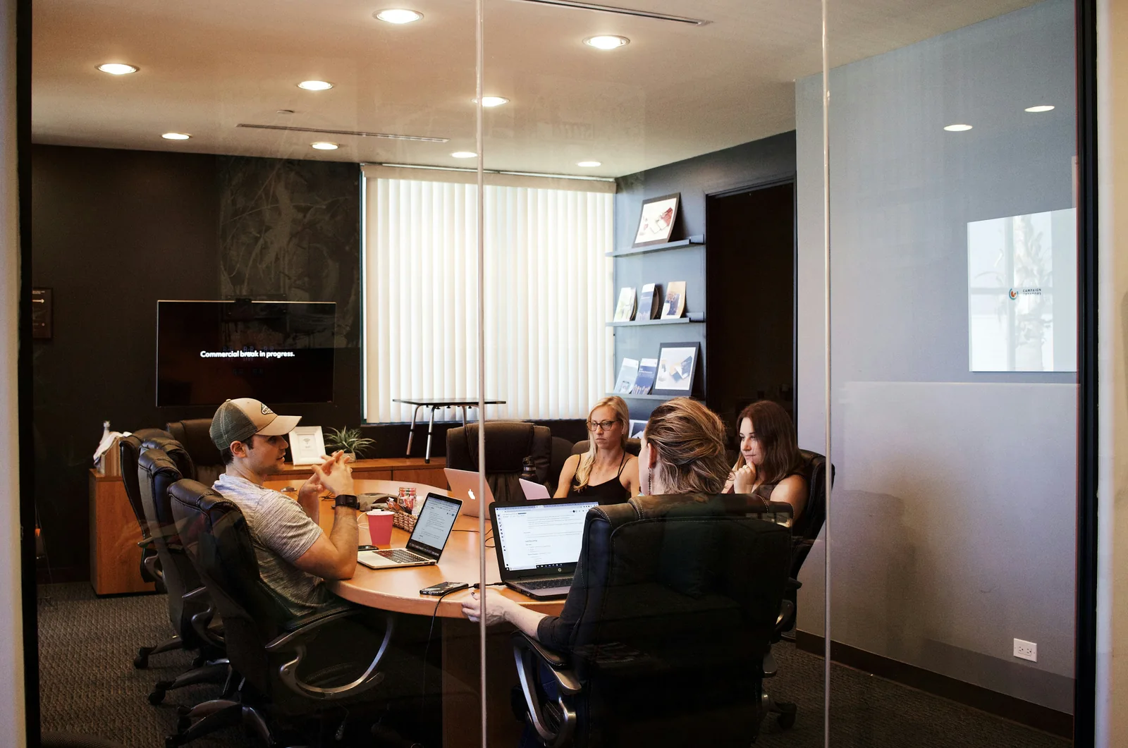 Colleagues leaning into a working discussion around a laptop and a wooden table.